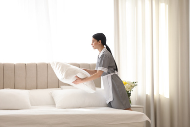 Young chambermaid making bed in hotel room