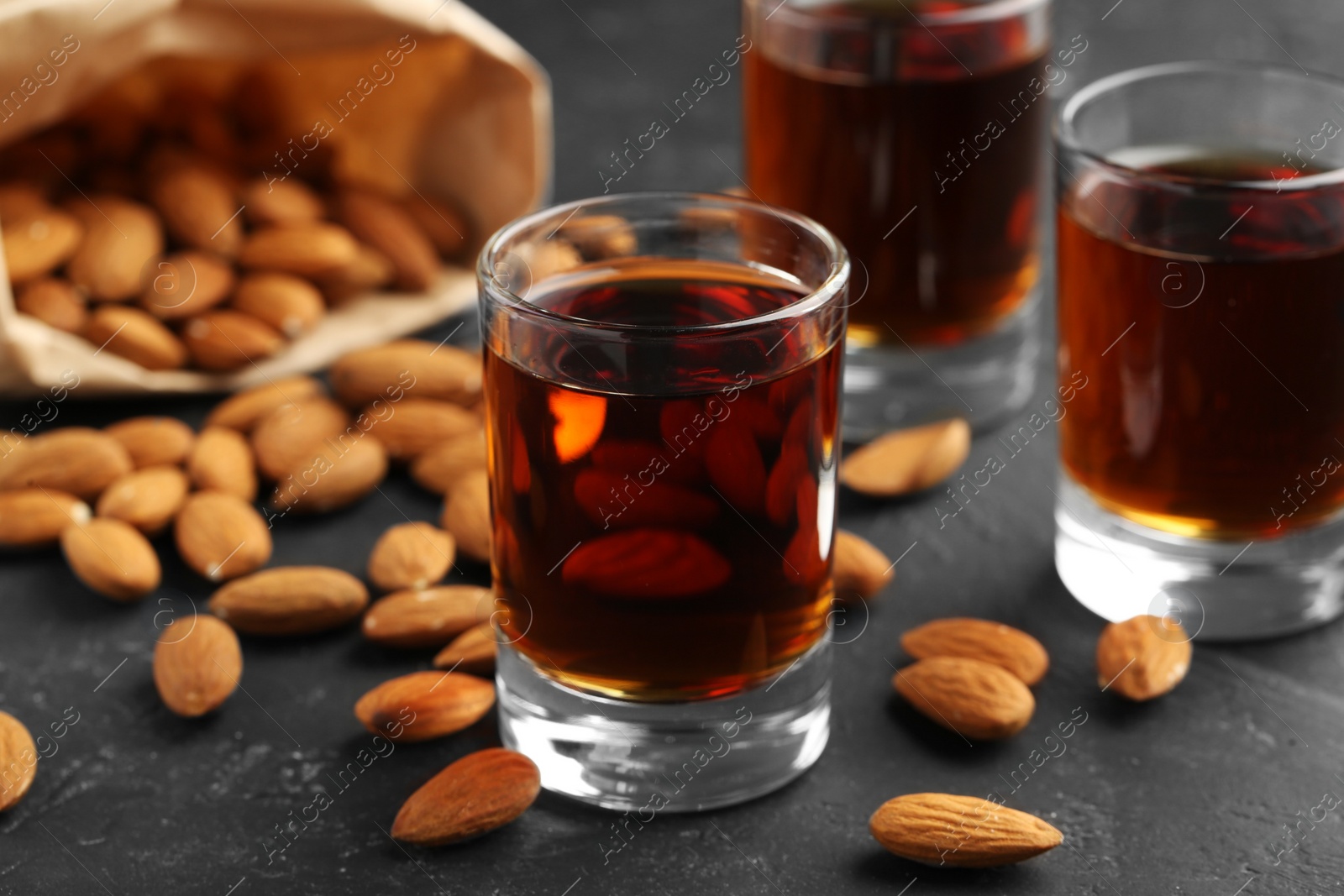 Photo of Glasses with tasty amaretto liqueur and almonds on dark gray table, closeup