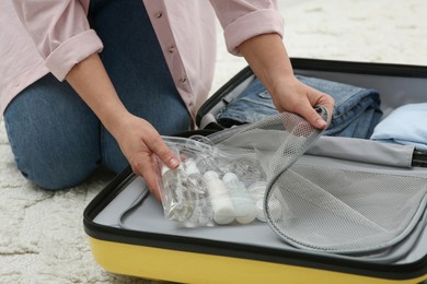 Photo of Woman with plastic bag of cosmetic travel kit packing suitcase, closeup. Bath accessories