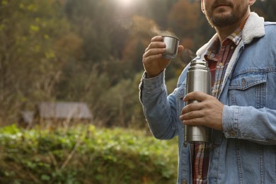 Photo of Man with metallic thermos and cup lid in nature, closeup. Space for text