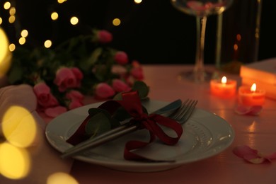 Place setting with roses and candles on pink wooden table, closeup. Romantic dinner