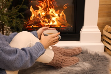 Photo of Woman with cup of tea sitting near burning fireplace, closeup