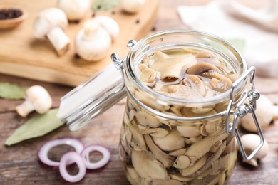 Photo of Glass jar of pickled mushrooms on table, closeup