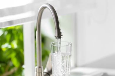 Photo of Filling glass with clear water from faucet indoors, closeup