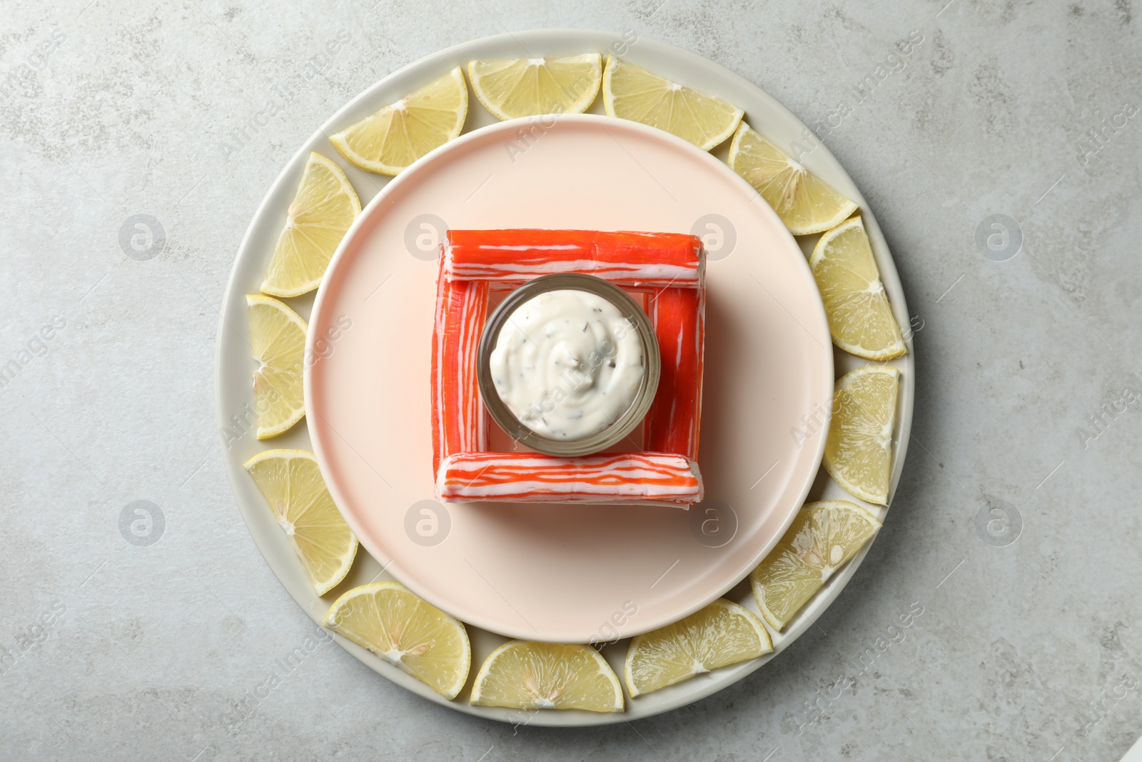 Photo of Crab sticks with sauce and lemon slices on light table, top view