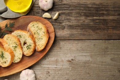 Photo of Tasty baguette with garlic, dill and oil on wooden table, flat lay. Space for text