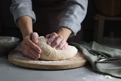 Woman kneading dough at grey table, closeup