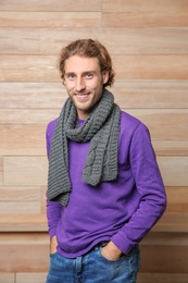 Handsome young man in warm sweater with scarf on wooden background