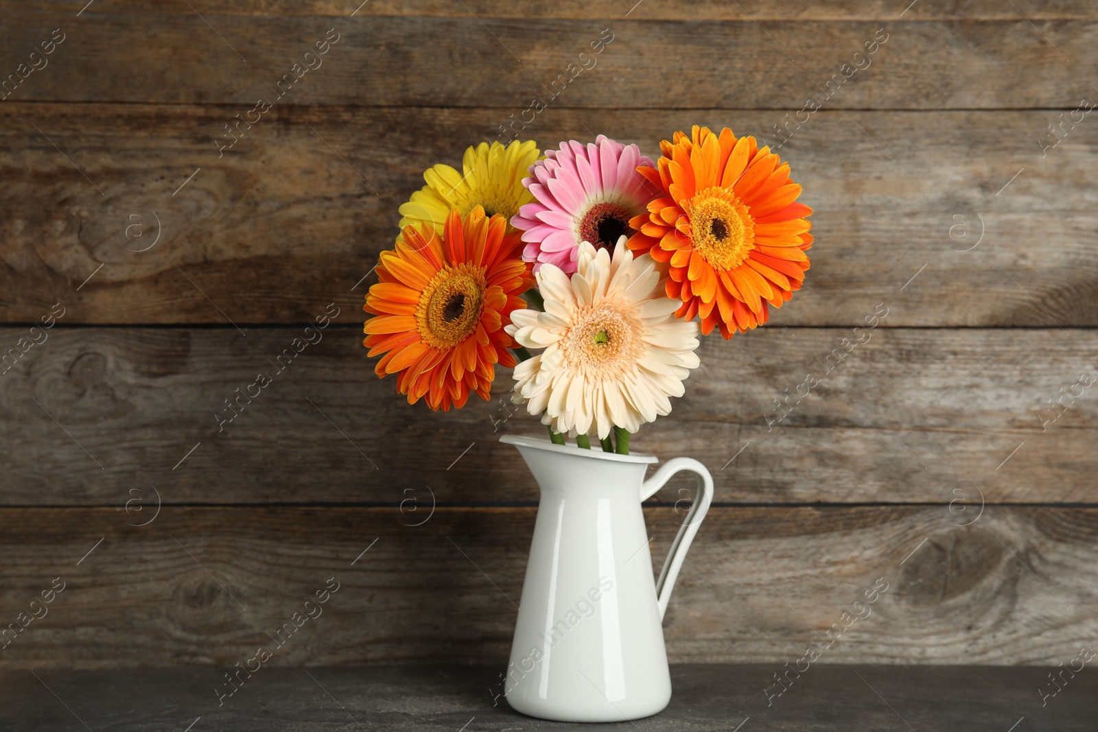 Photo of Bouquet of beautiful bright gerbera flowers in vase on table against wooden background