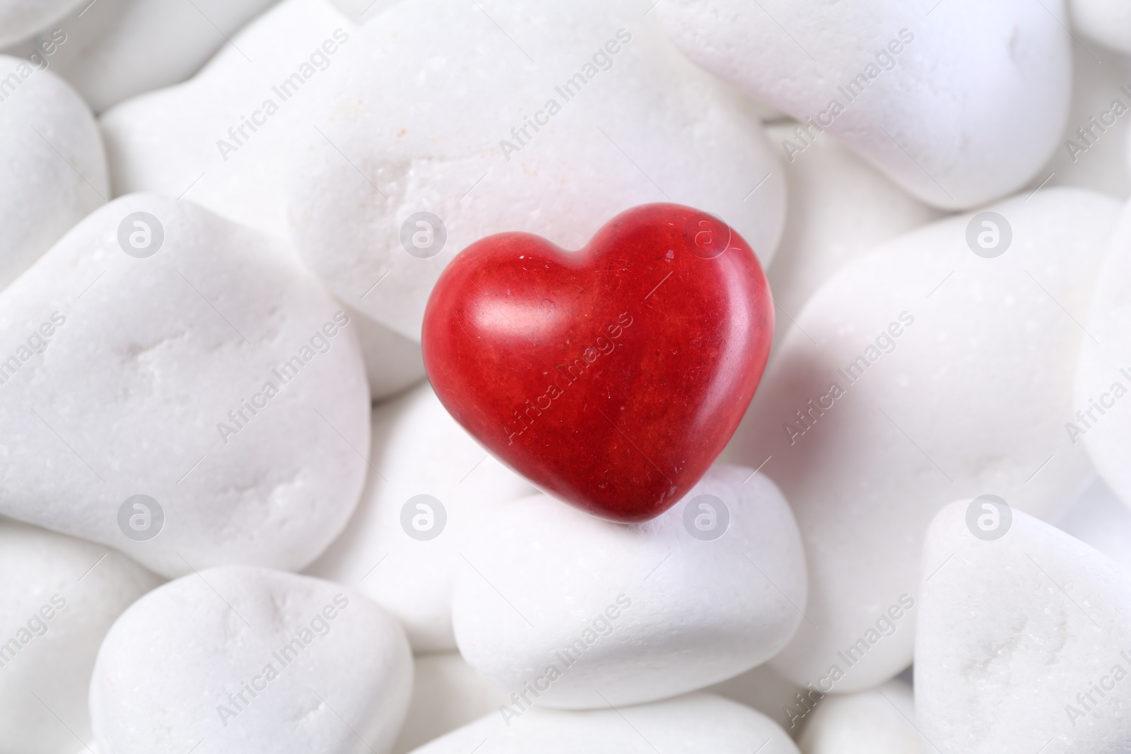 Photo of Decorative heart on white pebble stones, top view