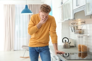 Photo of Young man having nausea in kitchen. Feeling sick