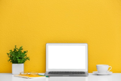 Photo of Modern laptop on desk near yellow wall, space for design. Home workplace