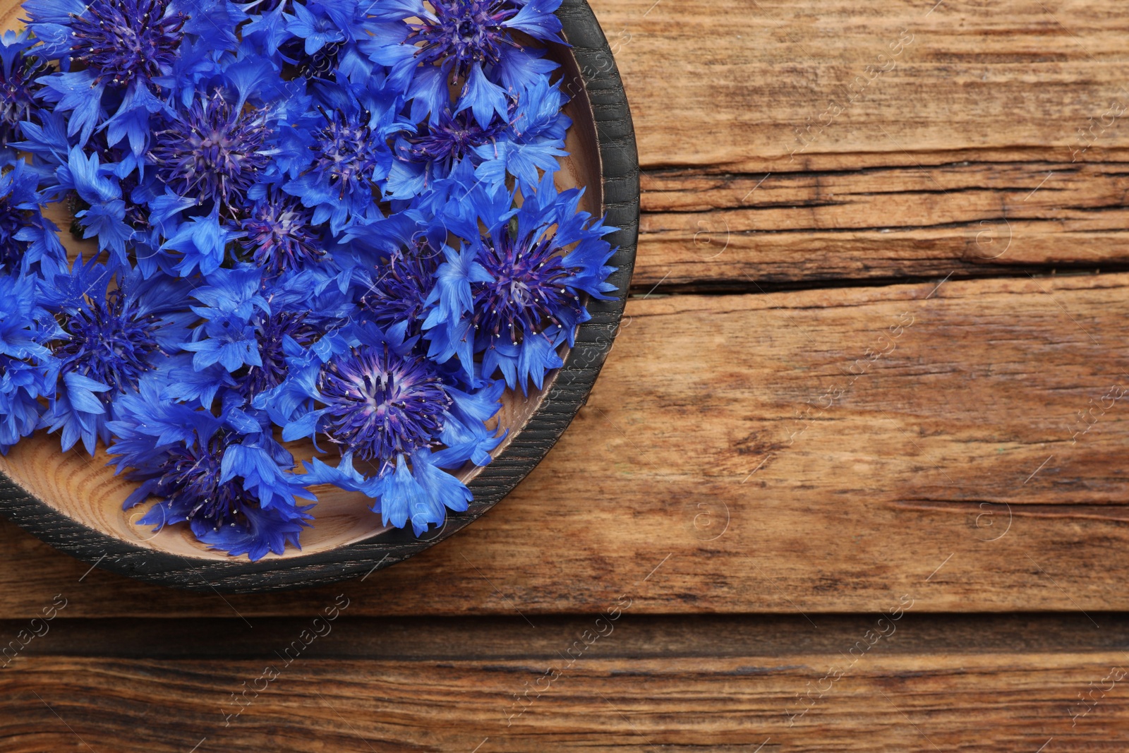 Photo of Beautiful blue cornflowers in bowl on wooden table, top view. Space for text