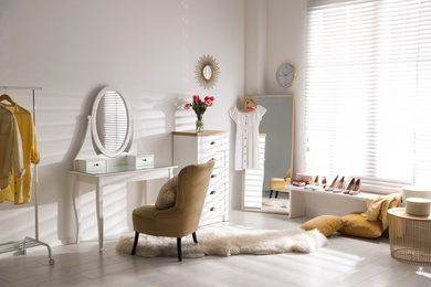 Stylish room interior with elegant dressing table, mirror and comfortable chair