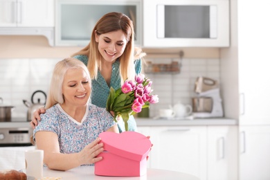 Daughter congratulating happy mature woman on Mother's Day at home