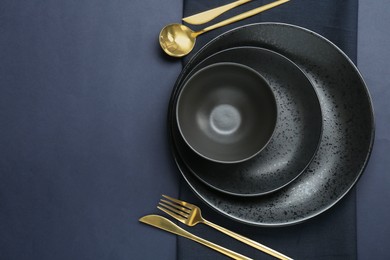 Stylish ceramic plates, bowl, cutlery and napkin on dark blue background, top view. Space for text