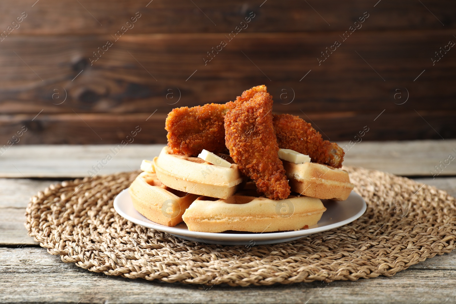 Photo of Delicious Belgium waffles served with fried chicken and butter on wooden table, closeup