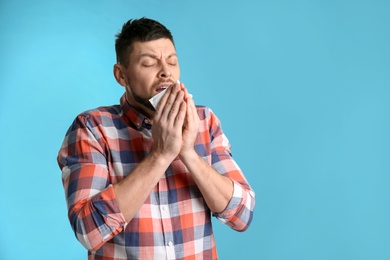 Man with tissue sneezing on light blue background, space for text. Runny nose
