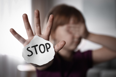 Abused little girl with sign STOP indoors, focus on hand. Domestic violence concept