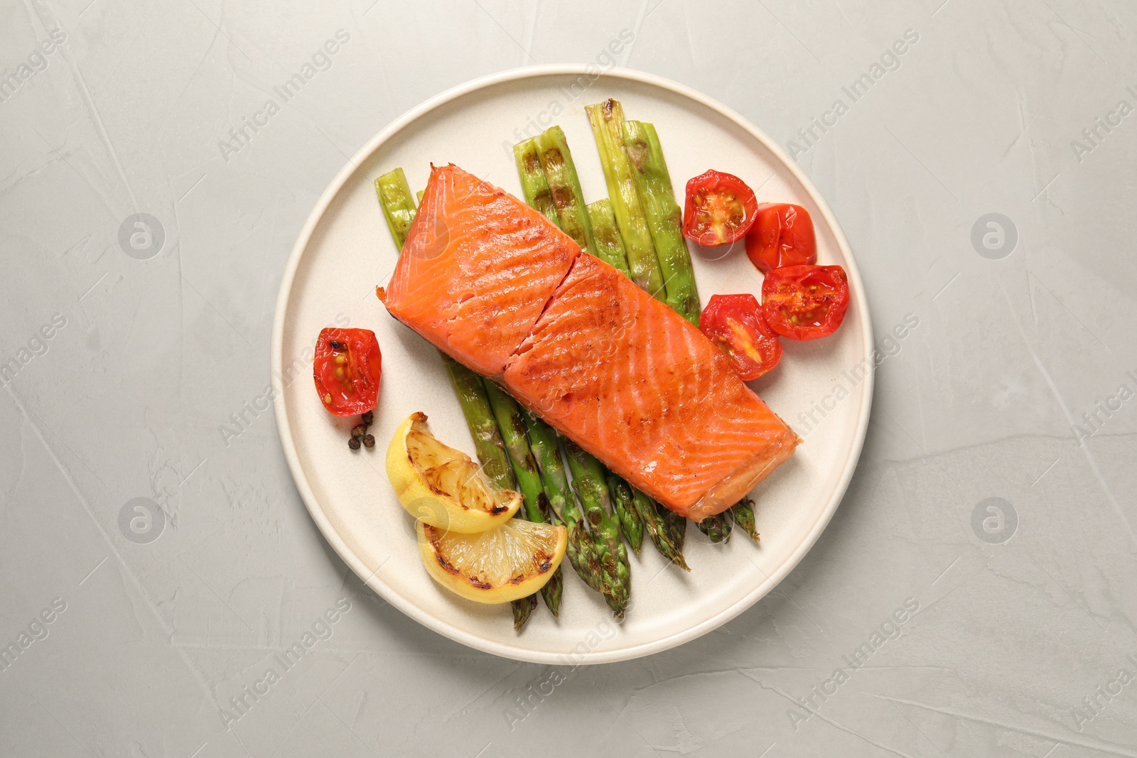 Photo of Tasty grilled salmon with asparagus, tomatoes, spices and lemon on light grey table, top view