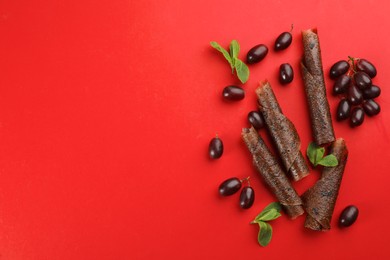 Photo of Delicious fruit leather rolls, mint and grapes on red background, flat lay. Space for text