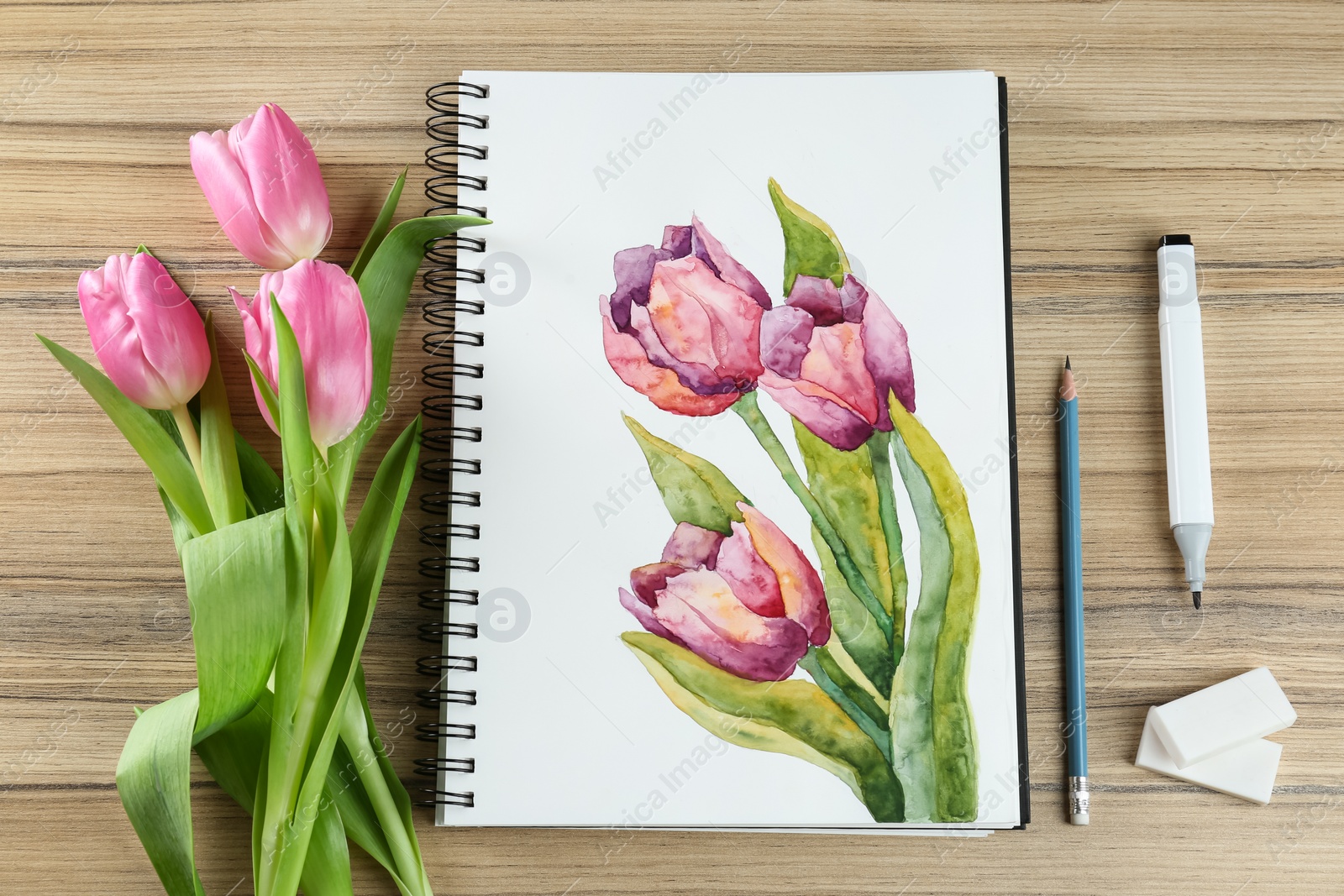 Photo of Painting of tulips in sketchbook, flowers and art supplies on wooden table, flat lay