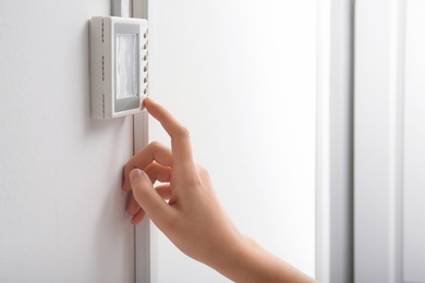 Photo of Woman adjusting thermostat on white wall, closeup. Heating system