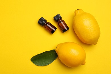 Photo of Bottles of citrus essential oil and fresh lemons on yellow background, flat lay