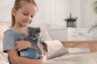 Cute little girl with kitten at home, space for text. Childhood pet