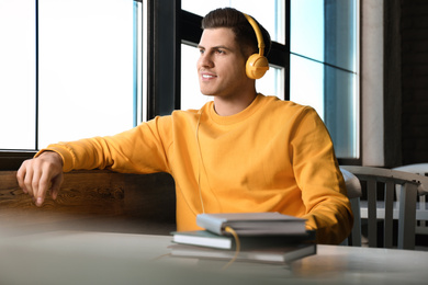 Photo of Man with headphones connected to book at table in cafe