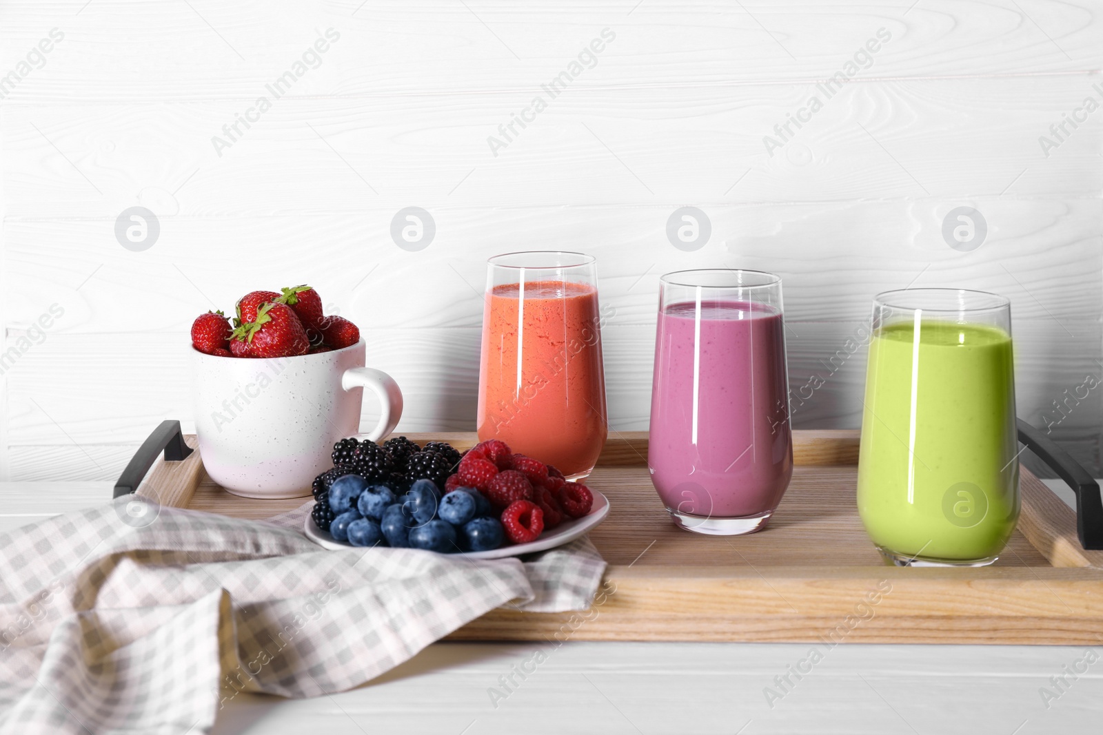 Photo of Glasses of different tasty smoothies and fresh ingredients on white wooden table