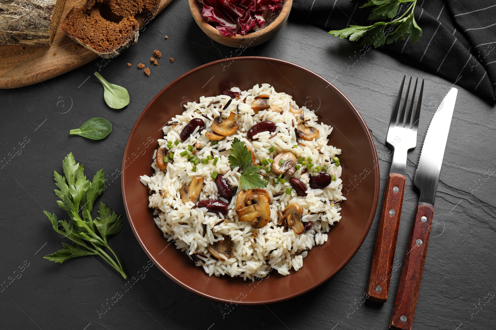 Photo of Delicious rice pilaf with mushrooms served on black table, flat lay