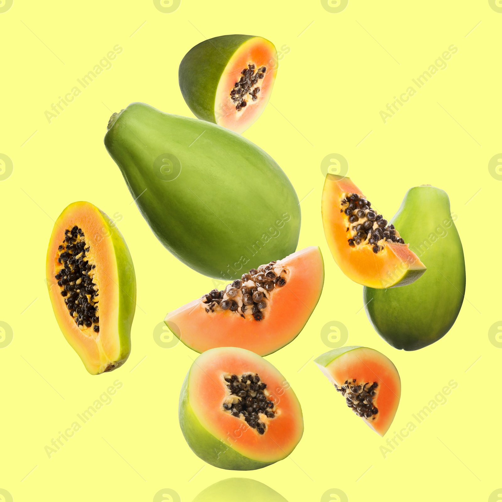 Image of Cut and whole papaya fruits falling on light yellowish green background