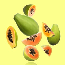 Image of Cut and whole papaya fruits falling on light yellowish green background
