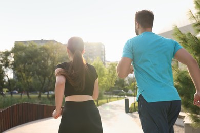 Healthy lifestyle. Happy couple running outdoors on sunny day, back view