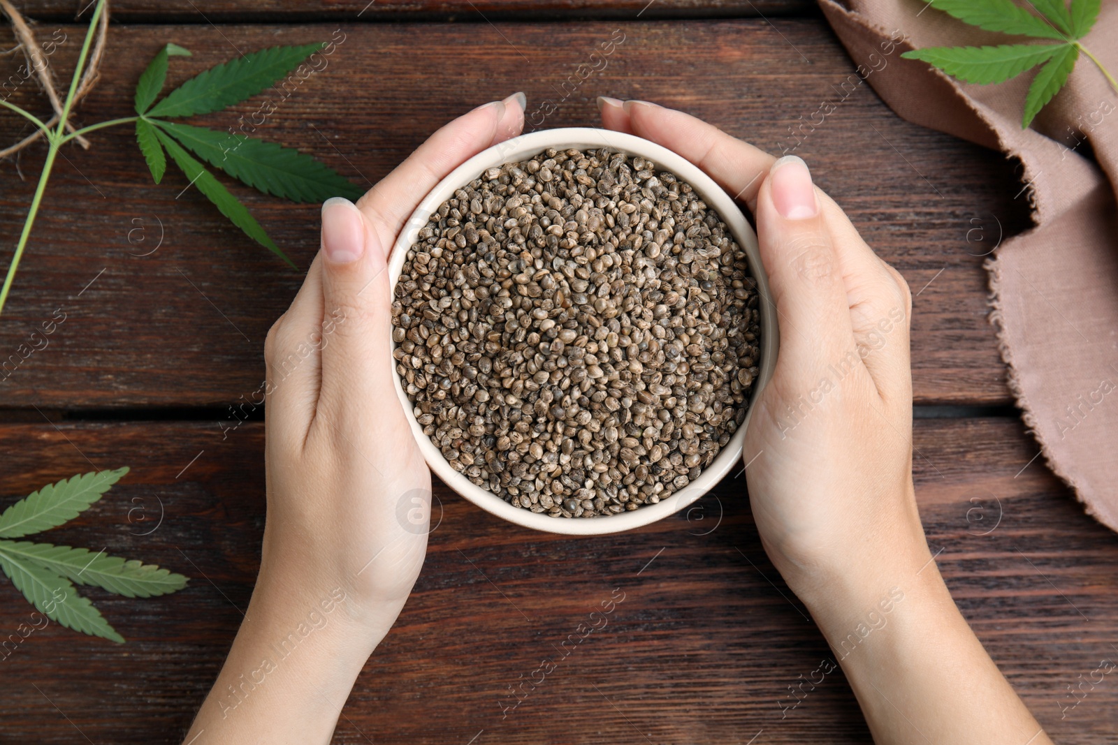 Photo of Woman holding bowl with hemp seeds at wooden table, top view