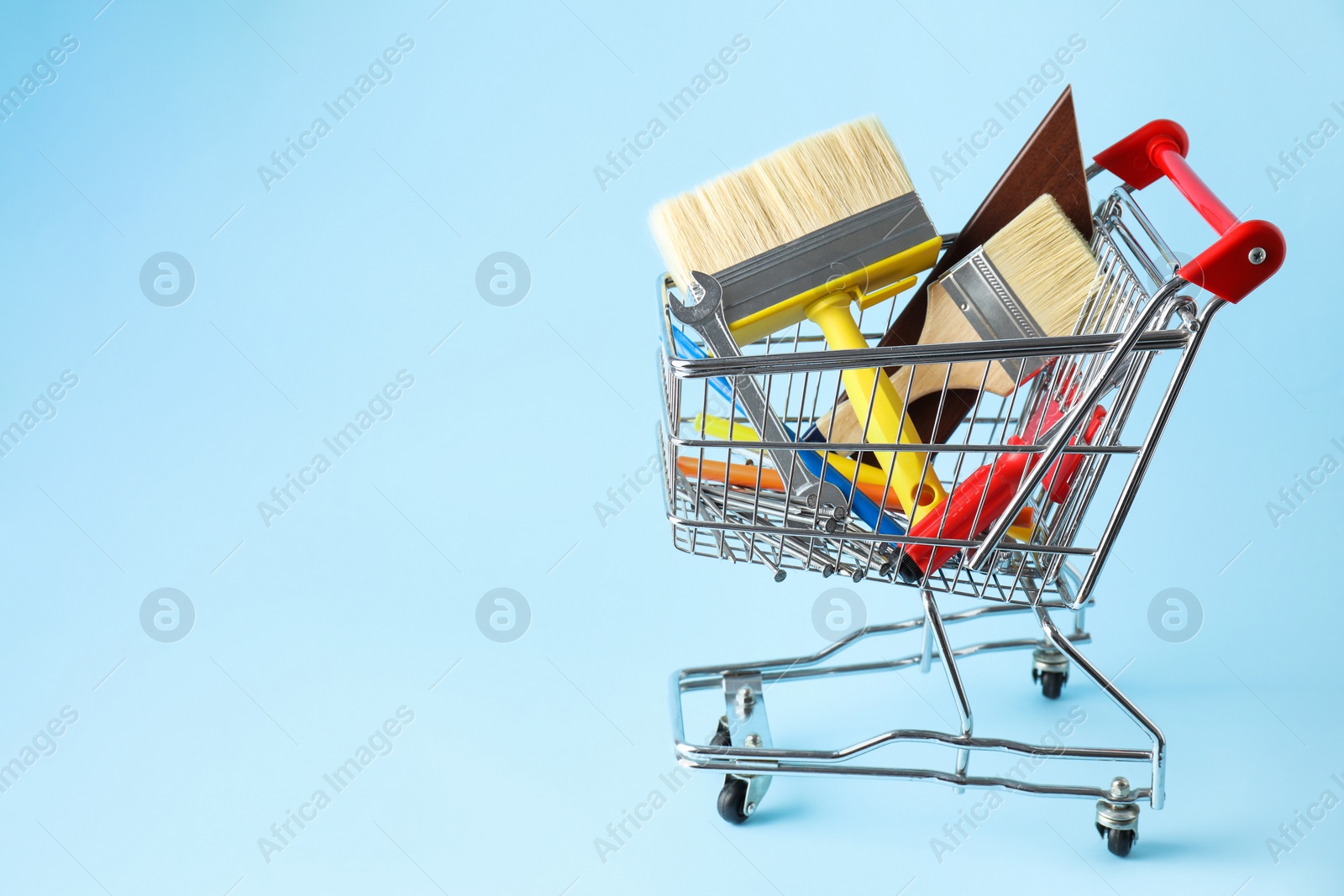Photo of Different construction tools in shopping cart on light blue background, space for text