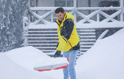 Man cleaning snow with shovel near house