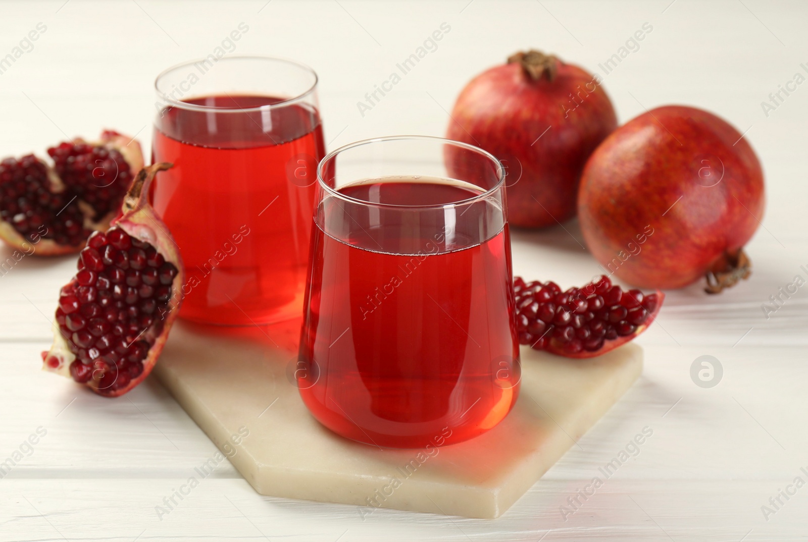 Photo of Tasty pomegranate juice in glasses and fresh fruits on white wooden table