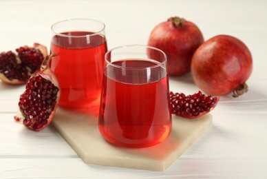 Photo of Tasty pomegranate juice in glasses and fresh fruits on white wooden table