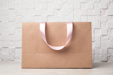 Photo of Paper shopping bag with ribbon handles on table near white wall. Mockup for design