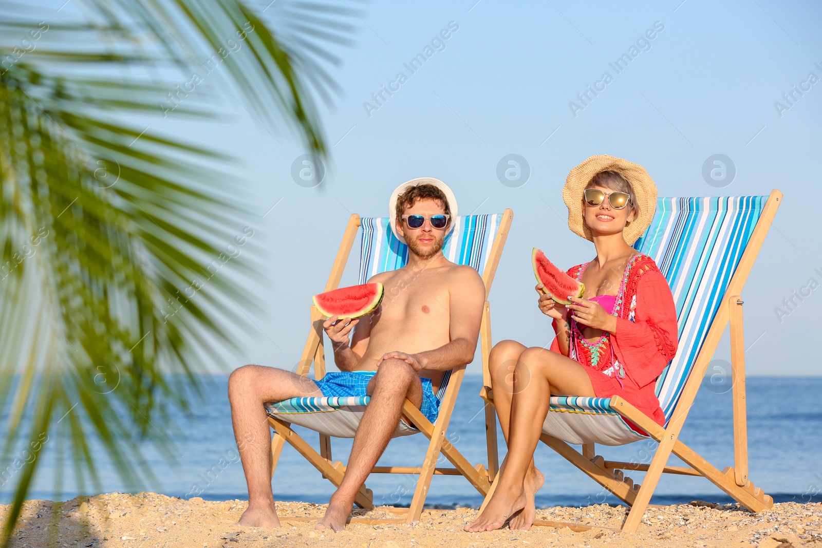 Photo of Young couple with watermelon slices in beach chairs at seacoast