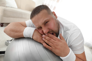 Lazy overweight man lying on exercise ball at home