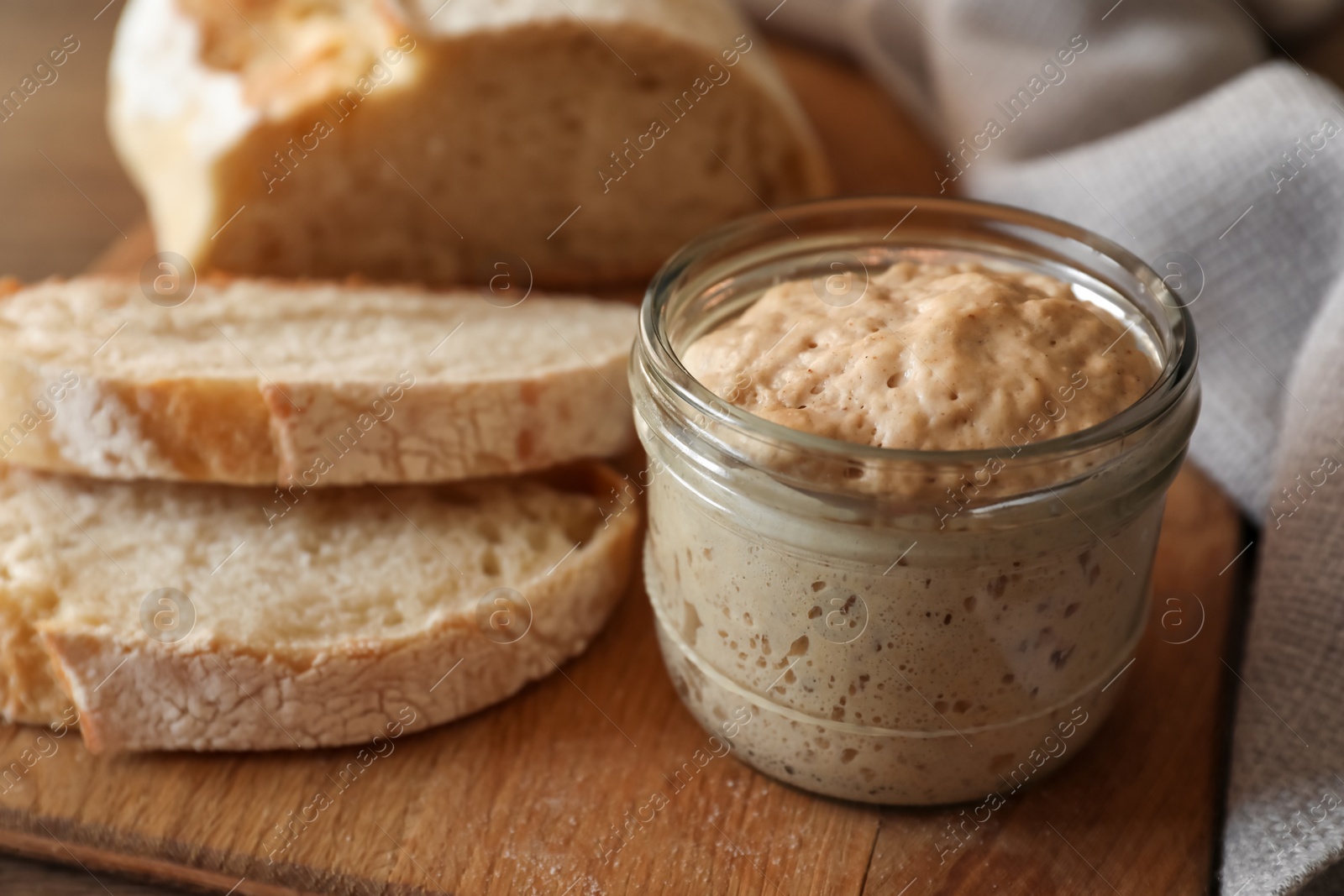 Photo of Sourdough starter in glass jar and bread on table, closeup