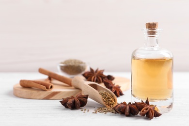 Bottle of essential oil, anise and seeds on white wooden table