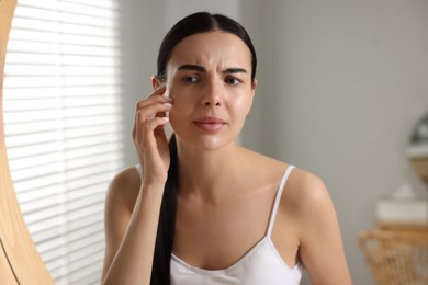 Photo of Woman with dry skin looking at mirror in bathroom