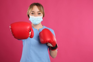 Photo of Doctor with protective mask and boxing gloves on pink background, space for text. Strong immunity concept