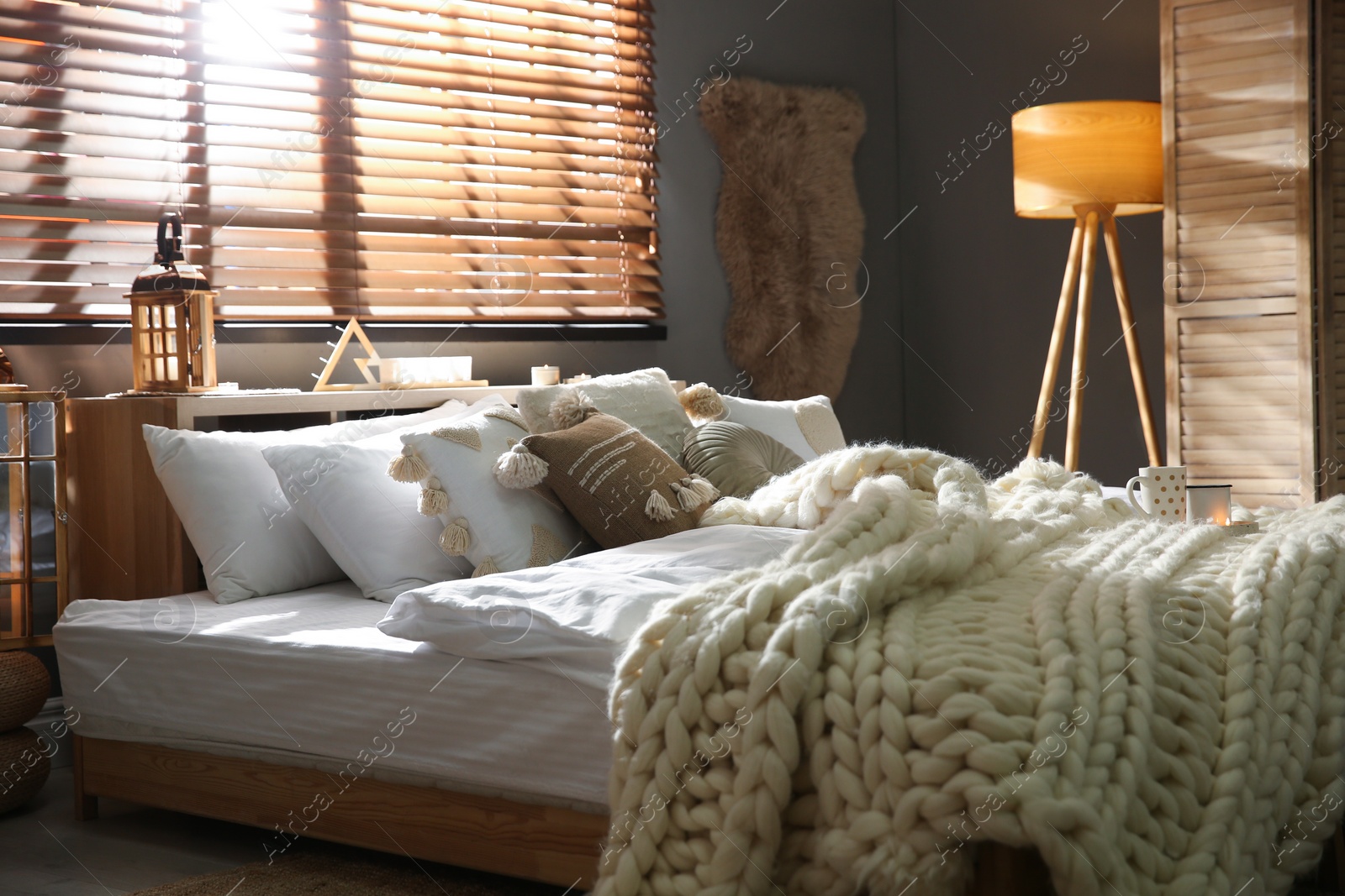 Photo of Cozy bedroom interior with knitted blanket and cushions