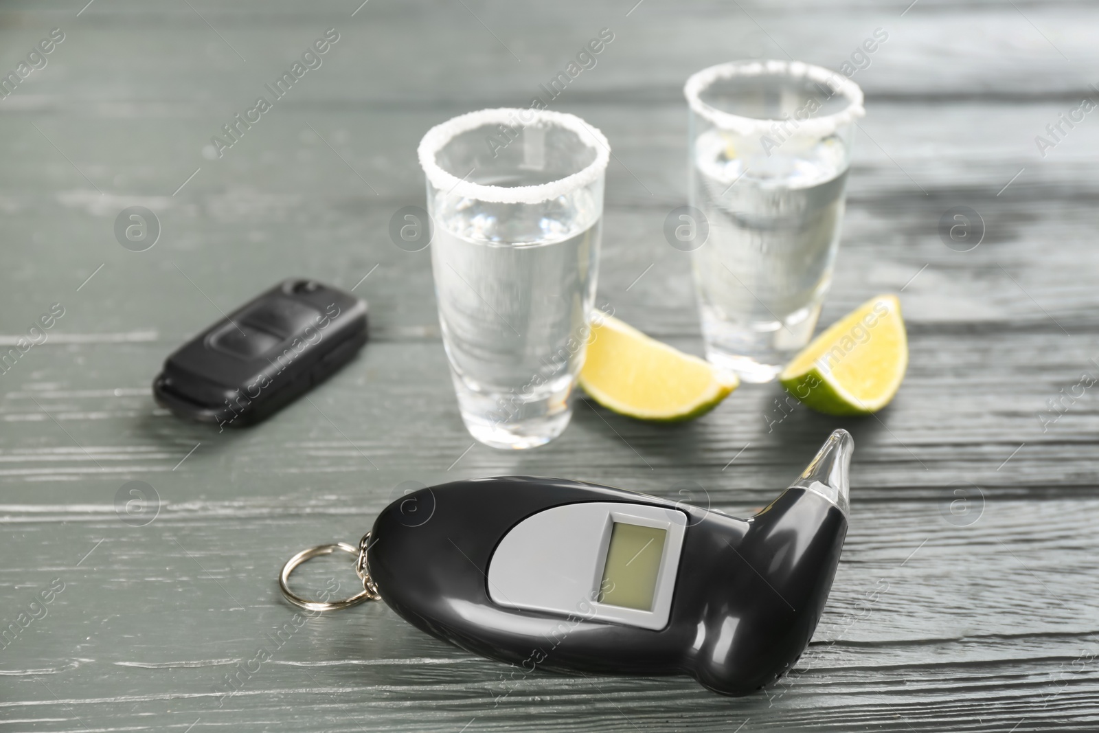 Photo of Modern breathalyzer, alcohol and car key on grey wooden background