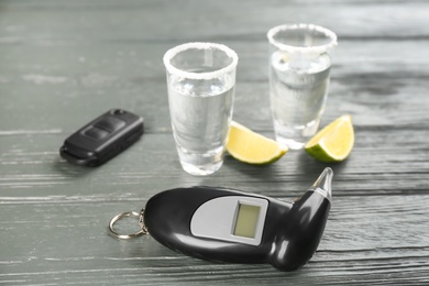 Modern breathalyzer, alcohol and car key on grey wooden background